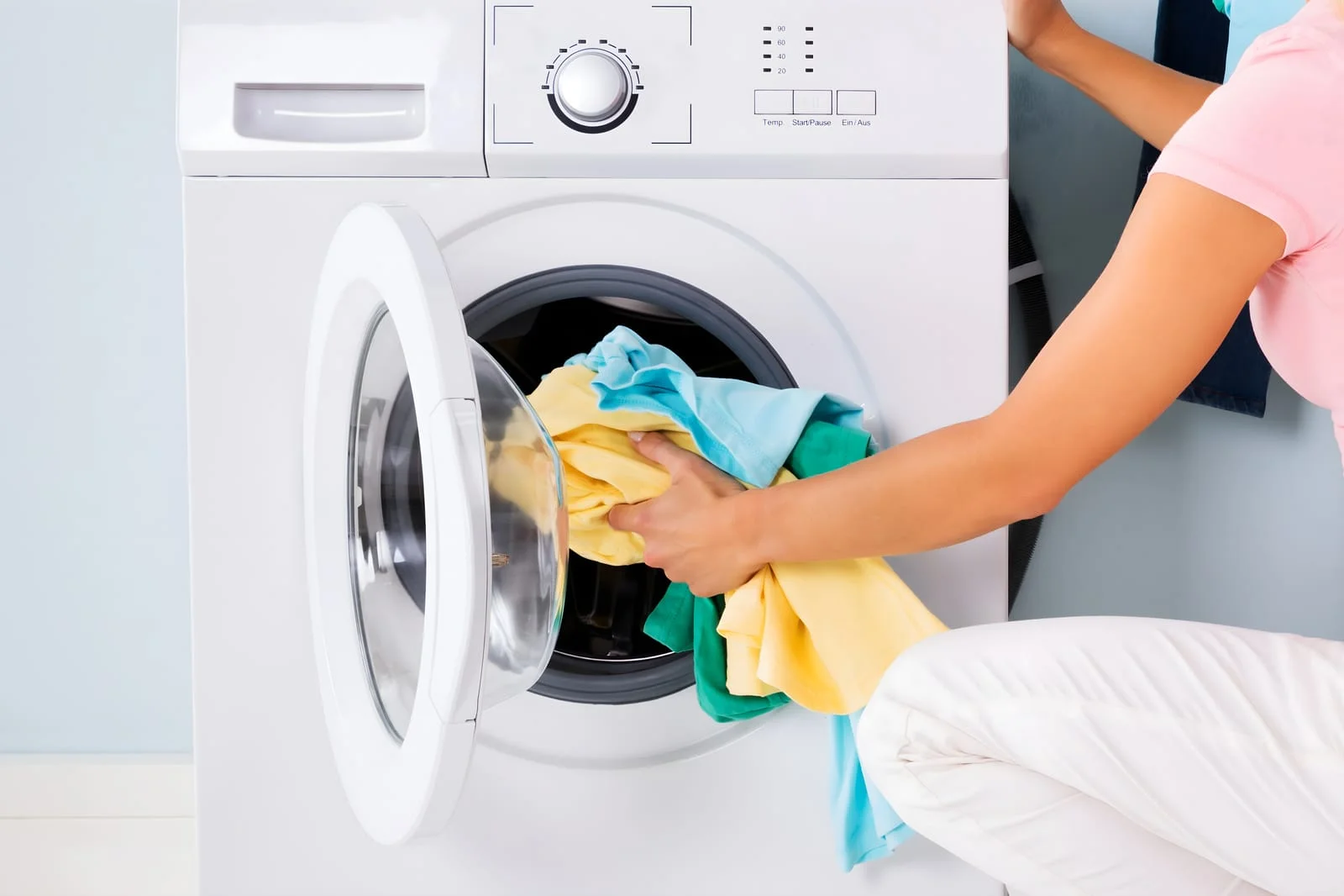 Washing Machine Maintenance Tips for Christmas - Appliance Repair Men - Appliance Repair Men - Appliance Repair Men A woman carefully loading a domestic washing machine with laundry to prevent motor strain and overloading during the busy Christmas period.