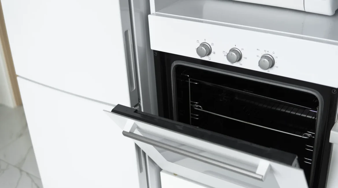Bottom Oven Element Failure and the Signs Hiding in Your Baking - Appliance Repair Men Engineer testing the bottom oven element of a built-in electric oven in a UK kitchen, floor panel lifted and multimeter in hand