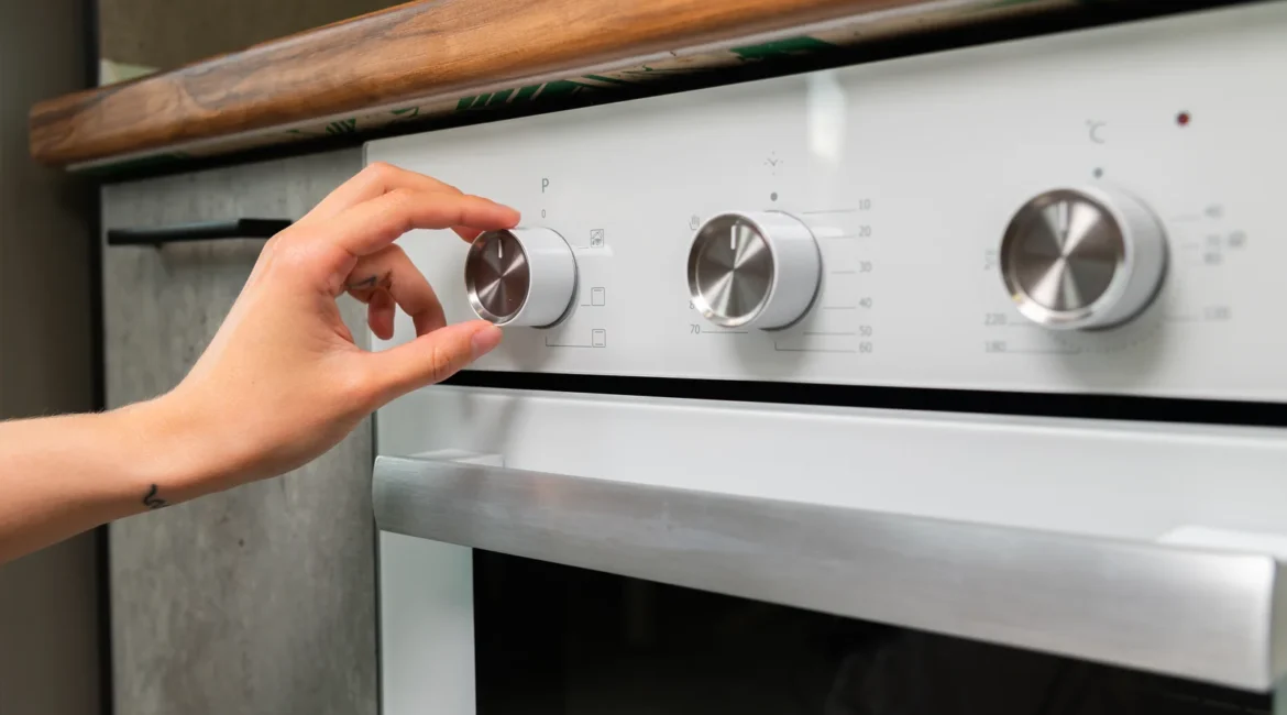 Engineer testing a cooker control switch behind the knobs of a freestanding electric cooker in a UK kitchen