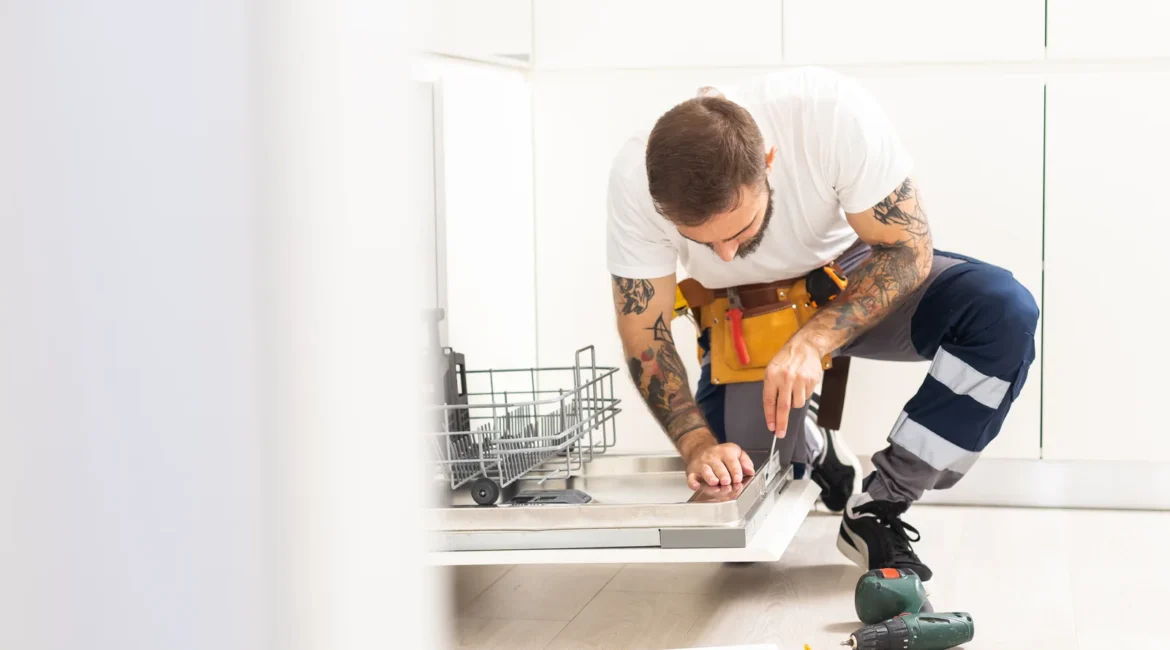 Dishwasher Leaking Water and What the Puddle Position Tells You - Appliance Repair Men Householder checking the kickboard of a dishwasher leaking water onto a tiled kitchen floor in a Formby home