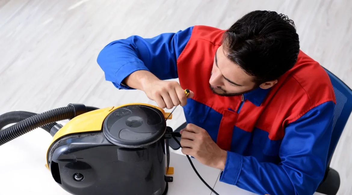 Engineer checking a vacuum cleaner overheating fault by removing the filter from a cylinder vacuum in a UK utility room