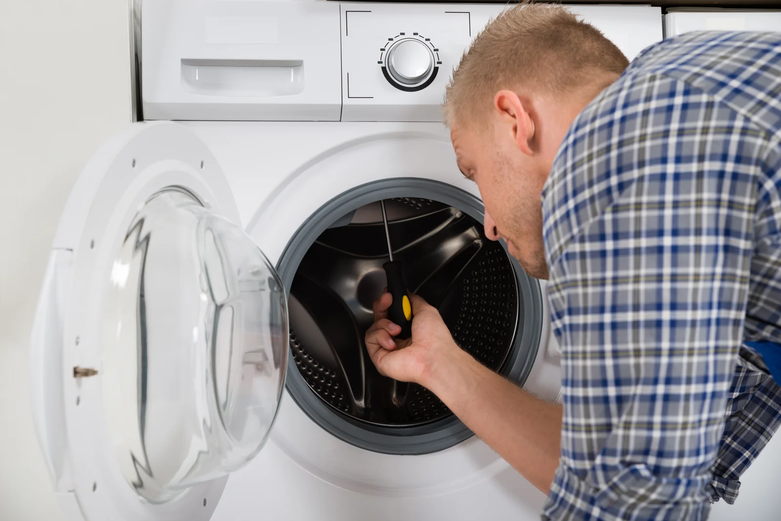 Washing Machine Drum Stuck and the Faults That Stop It Turning - Appliance Repair Men - Appliance Repair Men Engineer turning the drum by hand to check a washing machine drum stuck fault on a front loader in a UK utility room